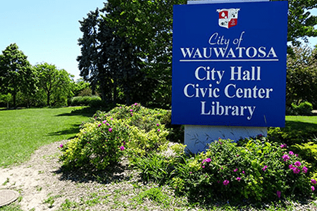 blue sign for the wauwatosa city hall with bushes and trees landscaped